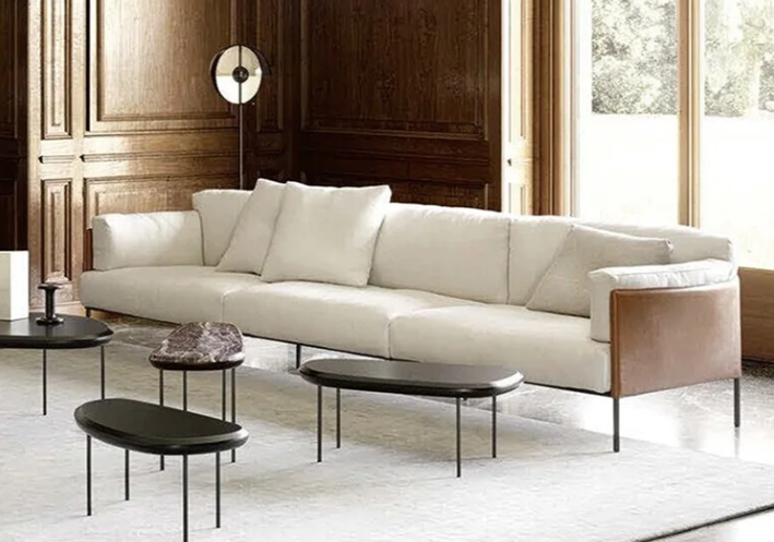 Greene sofa by David Lopez Quincoces with a tan saddle leather shell and plush off-white cushions, styled with low accent tables in an elegant wood-paneled living room.