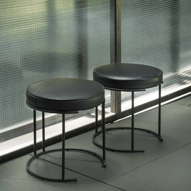 Nina stools in low and tall counter heights featuring round grey fabric upholstered seats supported by black tubular metal frames.