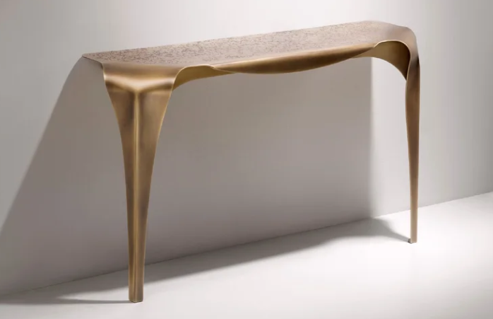 Sculptural Convivium console table featuring a fluid, draped brass metal silhouette with a textured top and slender tapered legs against a minimal background.