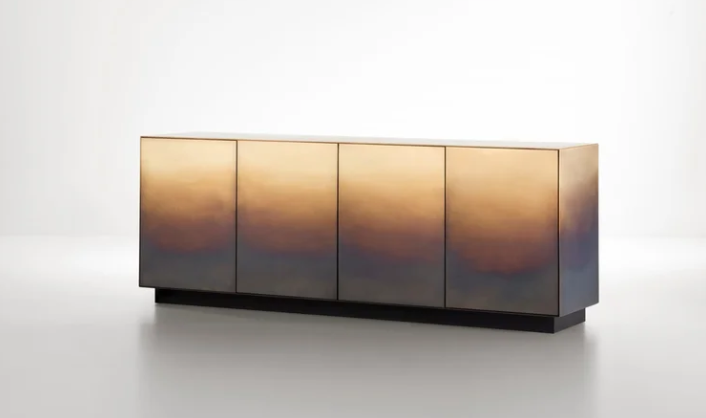 Modern Marea dresser featuring a metallic cabinet with four push-to-open doors with an ombré brass finish set on a dark recessed base against a bright background.