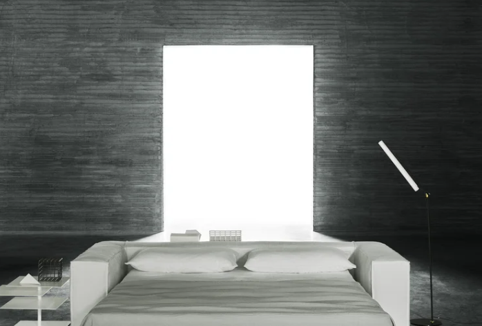 Neowall bed featuring a white upholstered platform with integrated headboard frame surrounding a bright window panel, set against dark textured walls with minimalist bedside tables and floor lamp in a monochromatic bedroom.
