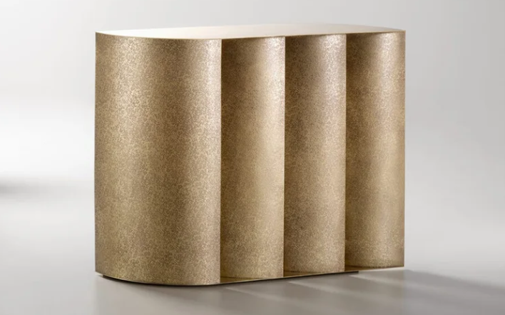 Sinestesia console table featuring a textured, metallic gold finish with a fluted, architectural column facade, isolated against a neutral background.