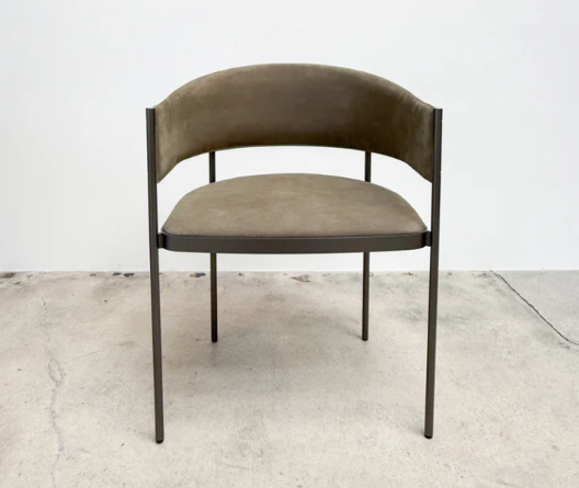 Stylish Era armchair featuring a slender dark metal frame with a curved olive brown suede backrest and matching cushioned seat, set on a plain concrete floor.