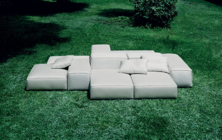 Extrasoft outdoor sofa featuring a low-profile modular seating arrangement in white upholstery, set directly on a grassy green lawn.