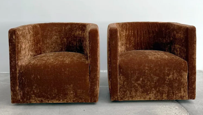 Confident swivel chairs featuring a rounded barrel silhouette fully upholstered in rich rust-brown crushed velvet, displayed as a pair against a minimal neutral background.