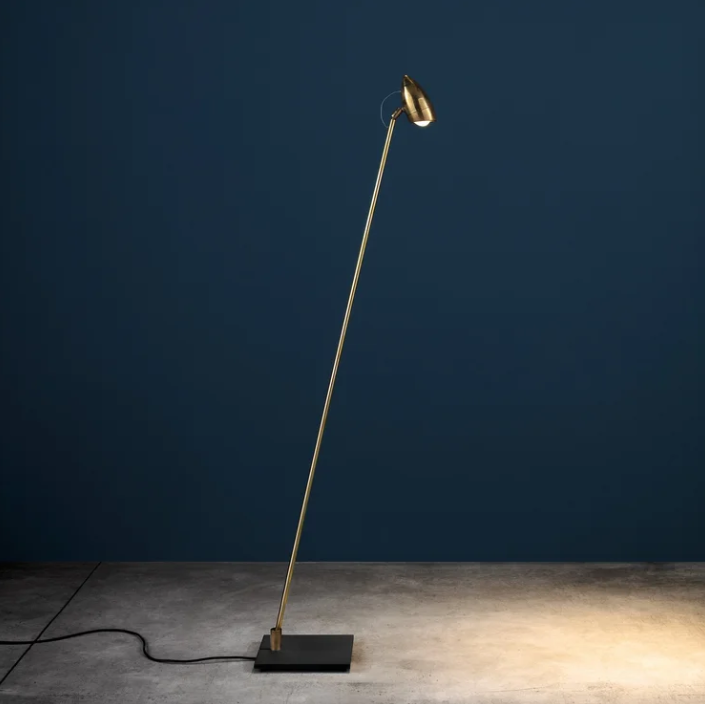Minimalist Cicloitalia floor lamp with a slender brass stem, adjustable spotlight shade, and a square black base set against a dark blue background.