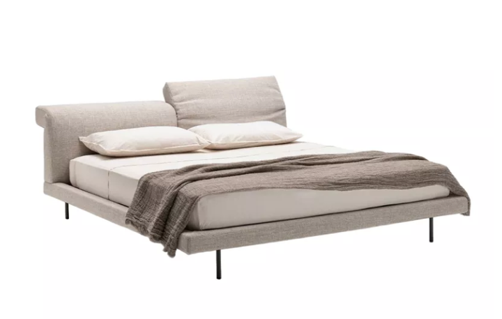 Contemporary Sumo bed featuring a slim upholstered frame on thin black metal legs, neutral textured fabric headboard, light bedding, and a draped brown throw.