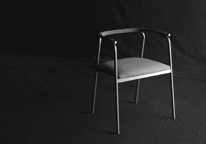Rivulet dining chair with gray upholstered seat and curved fabric backrest on a sleek metal frame with tapered legs, photographed against a black background.