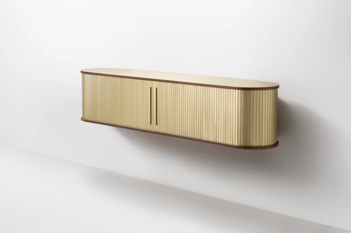 Modern wall-mounted floating console with rounded ends, featuring light-reflective, vertically ribbed golden metal sliding fronts set within a slender-edged frame against a minimalist white wall.