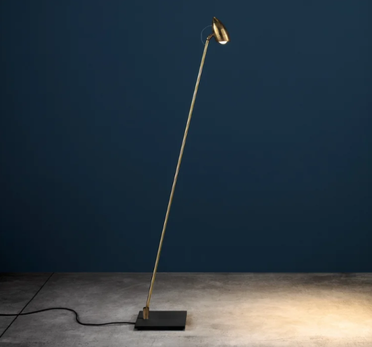 CicloItalia floor lamp featuring an angled brass stem with a vintage bicycle-headlight-inspired metal shade, anchored by a flat square base.