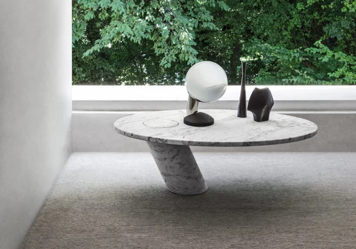 Eccentrico table displaying an elliptical white marble top balanced on an off-center angled cylindrical marble base, styled with a spherical lamp and decorative objects.