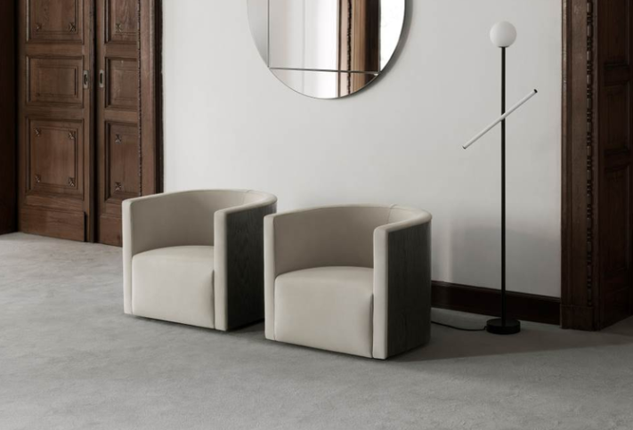 Confident lounge chairs with cream-colored upholstery and dark wood outer panels sit side-by-side on a gray carpeted floor.