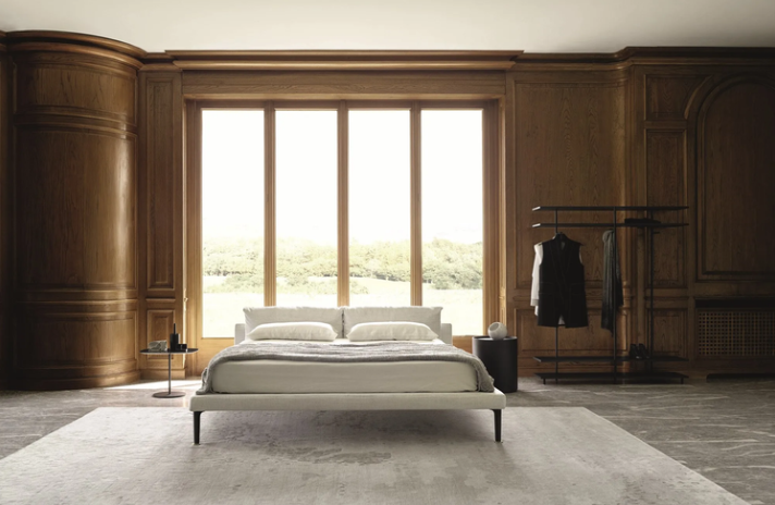 Floyd Hi bed featuring a thin upholstered platform frame in off-white with slender dark metal feet and double headboard cushions, positioned on a neutral area rug.