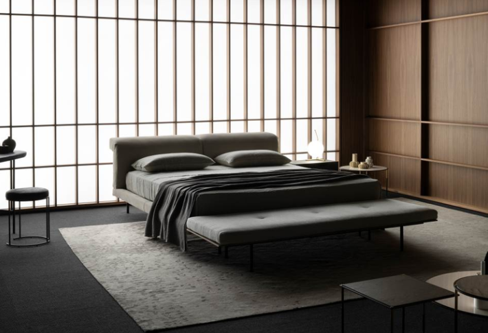 Stylish Sumo bed featuring a low-profile upholstered frame with a soft, curved headboard, set in a modern room with a shoji screen backdrop.