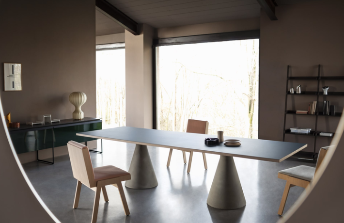 Modern Tavolo dining table featuring a long dark gray rectangular top supported by two conical concrete bases, styled with light wooden chairs in a spacious interior.