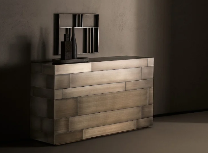 Modern-style Celato dresser featuring a metallic patchwork design of geometric brass panels, styled with minimalist decorative objects in a moody interior.