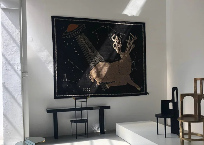 The Night of a Hunter rug by Rooms Studio features a stag with antlers being abducted by a UFO against a starry night sky with constellations.