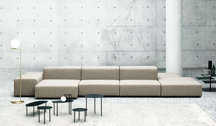 Extra Wall modular sectional sofa upholstered in light beige fabric, featuring rectilinear block seating and low backrests set against a concrete wall.
