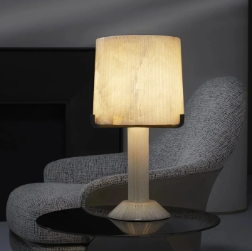 Acropolis table lamp by CTO Lighting featuring a white alabaster body with black steel accents on a side table, providing warm ambient lighting.
