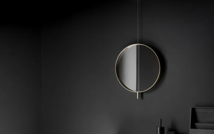 Contemporary Galileo round mirror framed in brass, suspended by a slender vertical cable against a matte black wall.