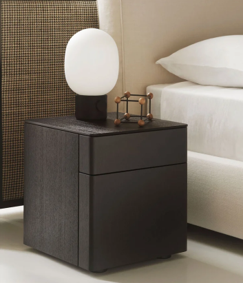 Byron Comodino nightstand featuring a dark wood cubic frame with integrated drawers, styled with an oval white table lamp next to a cream upholstered bed frame.