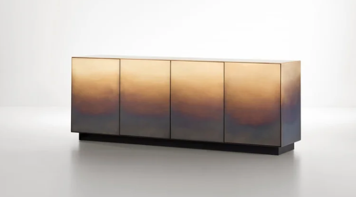 Marea dresser featuring a gradient brass finish with ombre shading across its four doors, set on a low dark plinth base.