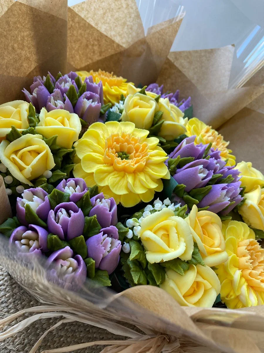 Bouquet of frosting flowers with yellow roses and purple tulips, wrapped in brown paper.