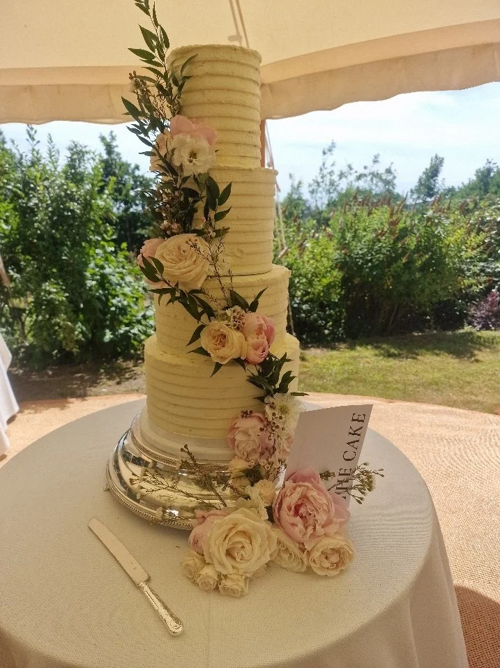 Four-tier ribbed buttercream wedding cake with a waterfall of fresh pink and cream roses, at a marquee wedding at home