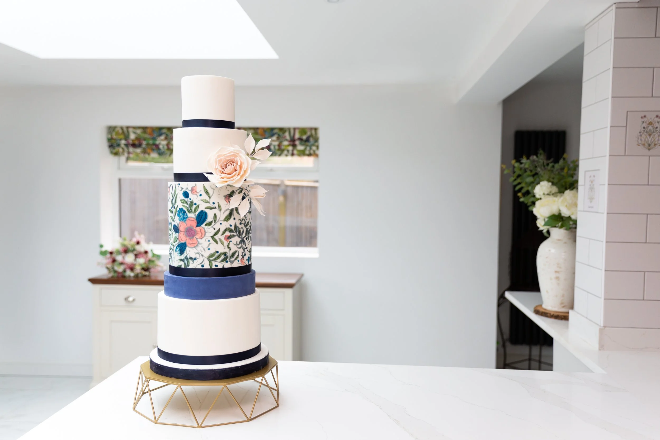Four-tiered wedding cake with floral and blue ribbon decorations on a marble counter.