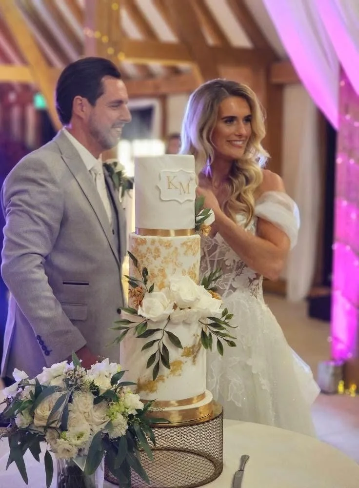 Karen and Matt cutting their four-tier white and gold wedding cake at Old Kent Barn