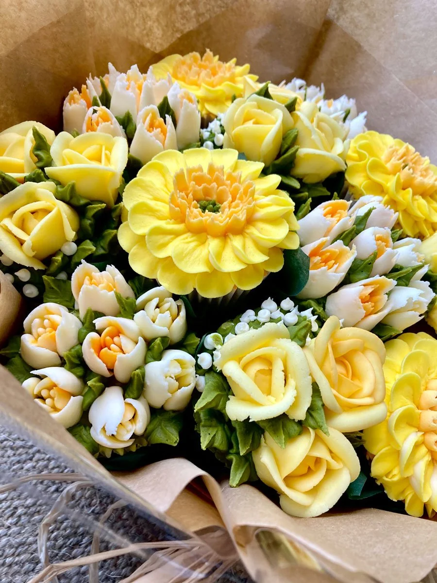 Bouquet of intricately crafted yellow and white buttercream flowers with green leaves on a brown paper background.