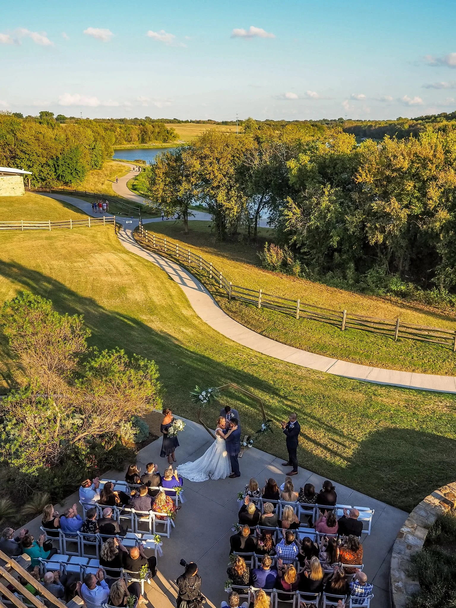 Ariel view of a wedding ceremony taking place on the back patio at The Nature & Retreat Center. The water and tree line featured in the background