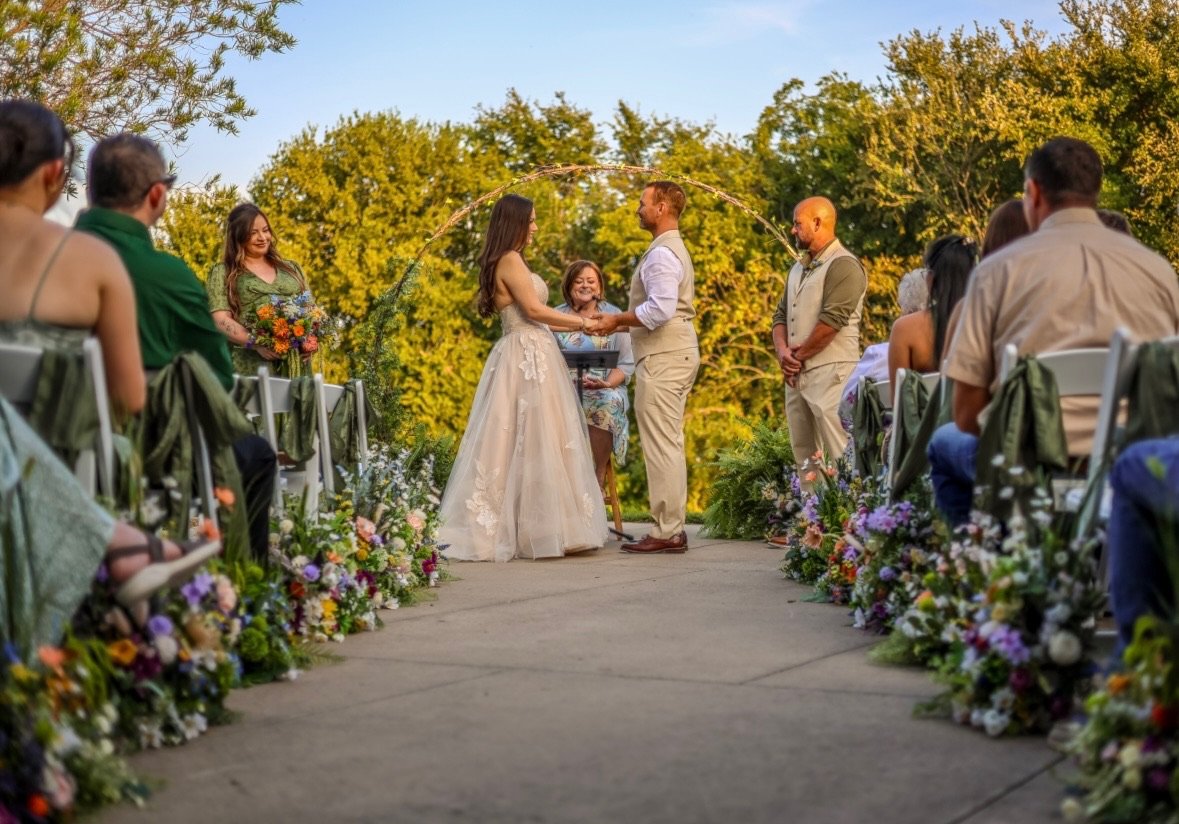 Bride and Groom at their wedding ceremony taking place at The Nature & Retreat Center outside on the back patio with the tree line in the background