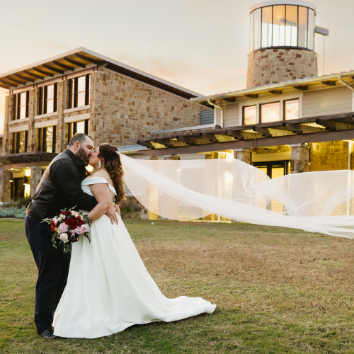 Bride and groom kissing after wedding ceremony during golden hour with The Nature & Retreat Center in the background.