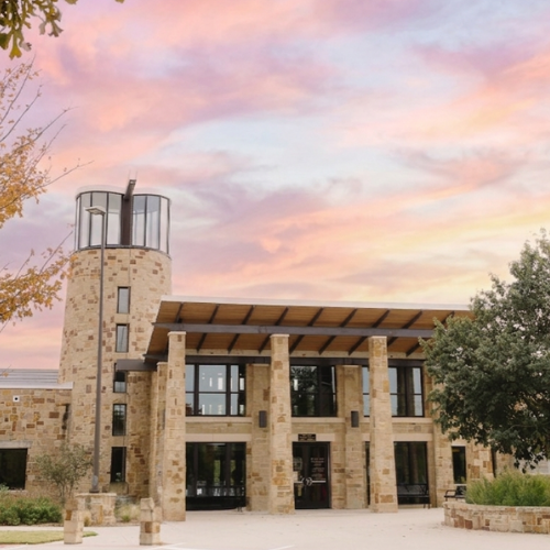 Exterior of building at sunset. Building features include a stone tower and floor to ceiling windows