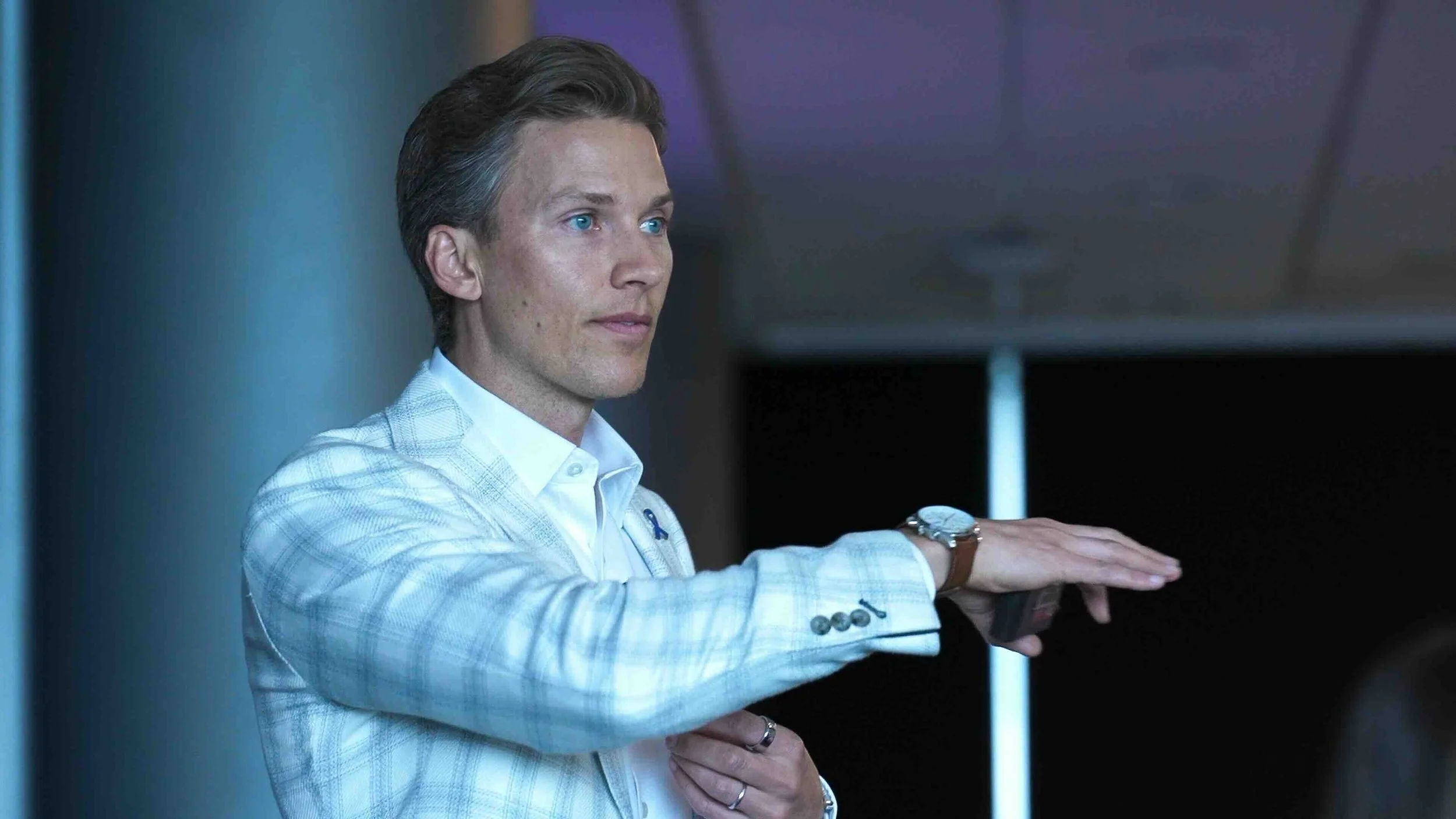 Keynote speaker Chris Rollins in a white blazer and shirt playing the piano, with a focus on his face and hands, in a modern indoor setting.