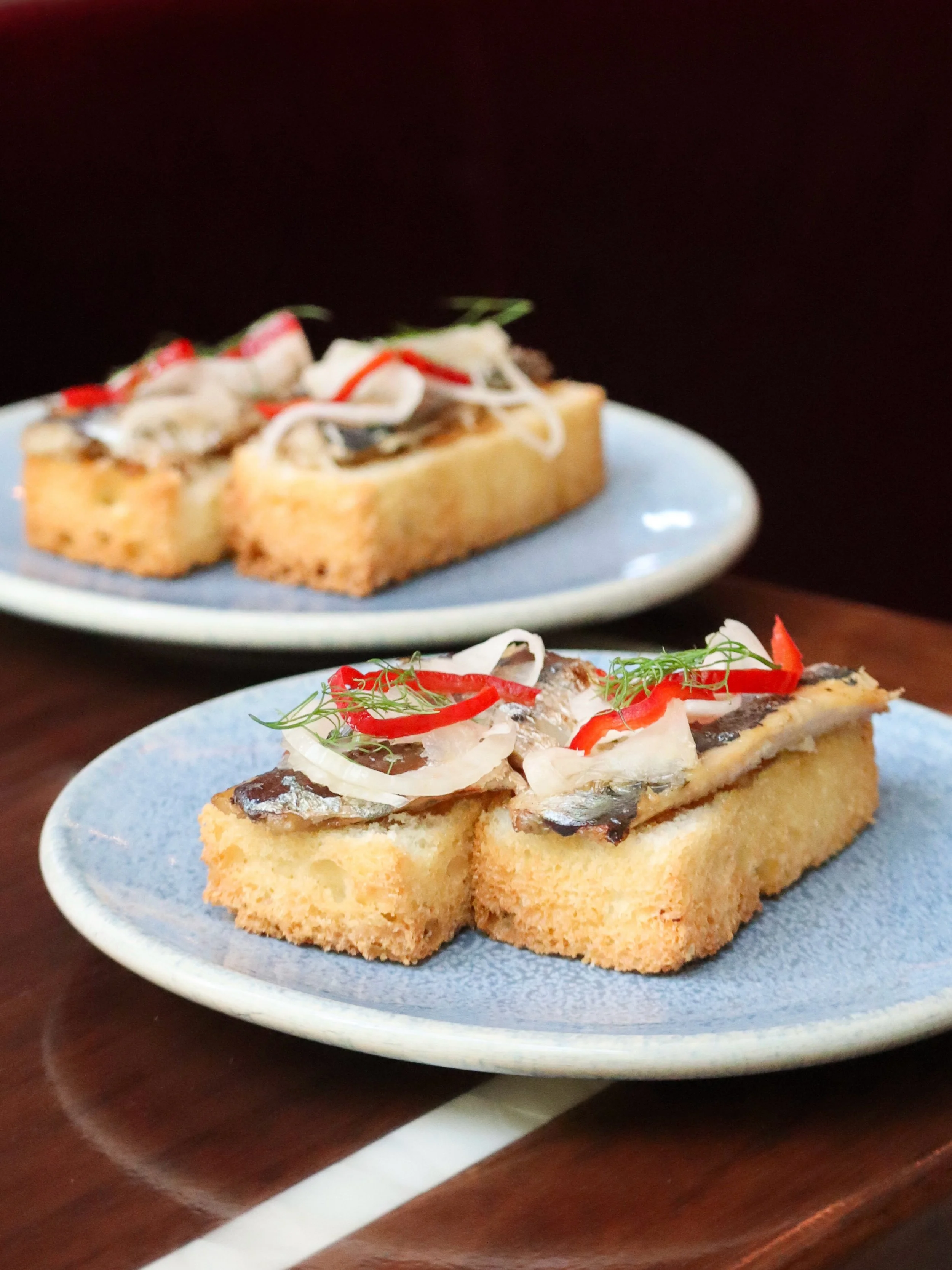 Sardine Toast layers house-made sardines over buttery brioche brushed with roasted garlic, finished with pickled peppers and fresh herbs. Crisp, savory, and bright, it captures the coastal character of Sicily, all in a few bites made for aperitivo.
