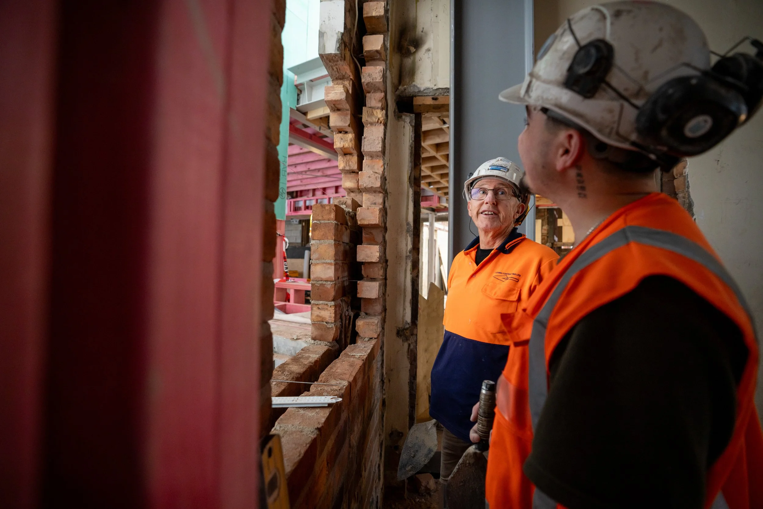 Two construction workers in orange safety vests and helmets having a conversation on a building construction site.