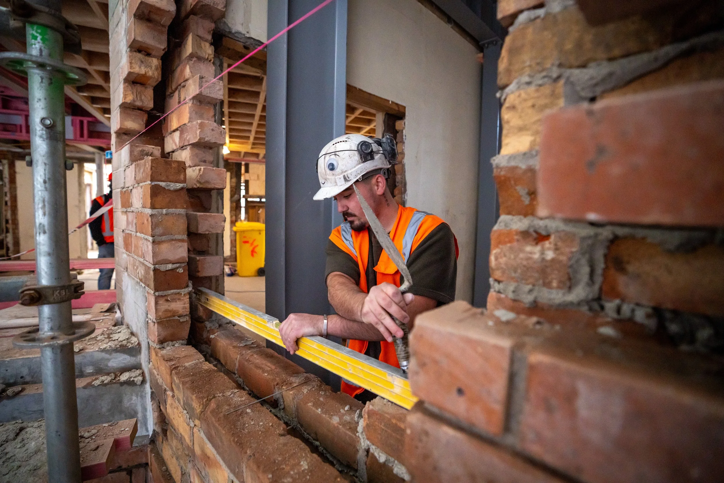 Construction worker measuring a brick wall with a level on a construction site.