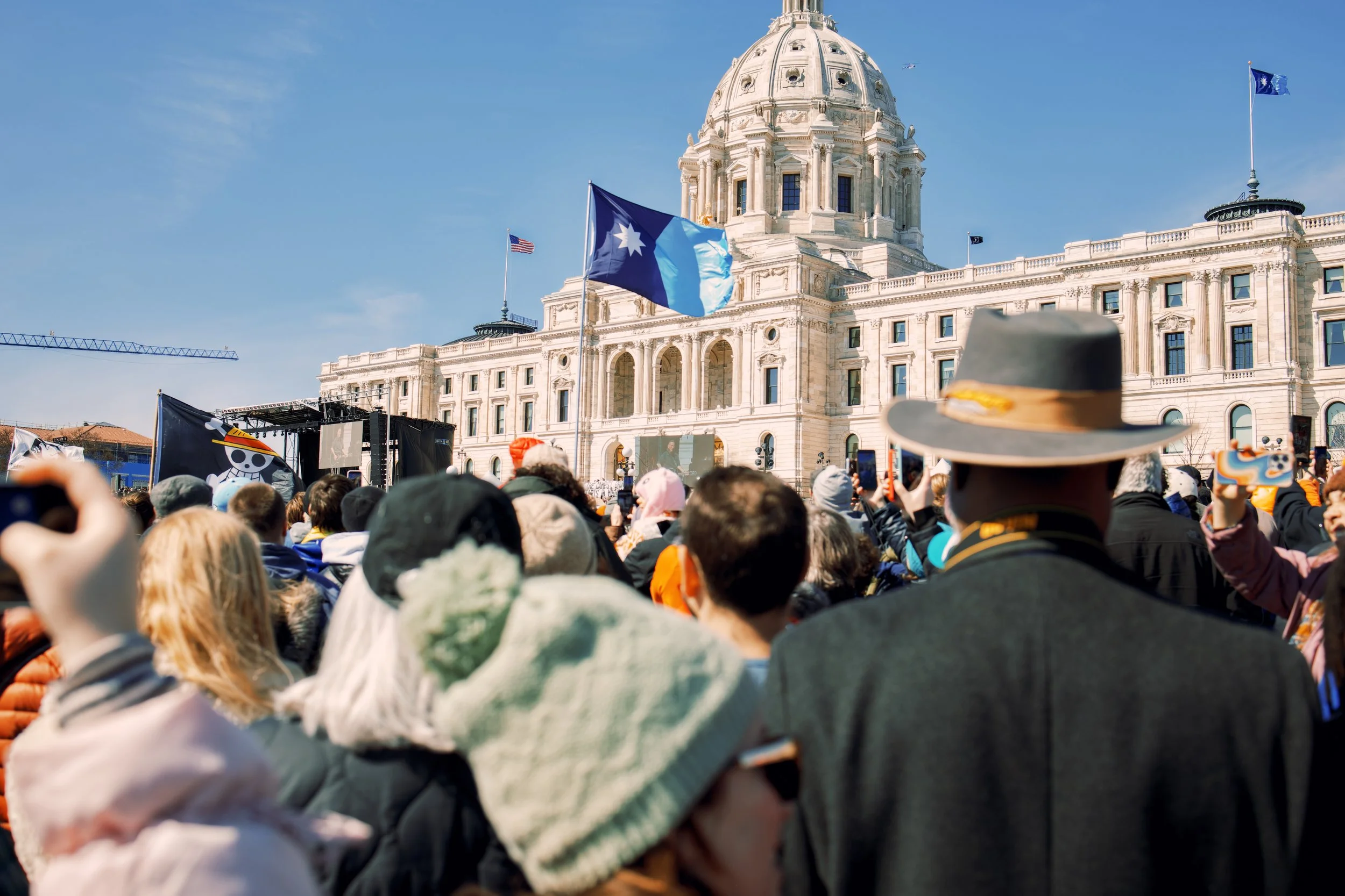 Crowd gathered outside the Minnesota State Capitol flying the new state flag during a sunny day.