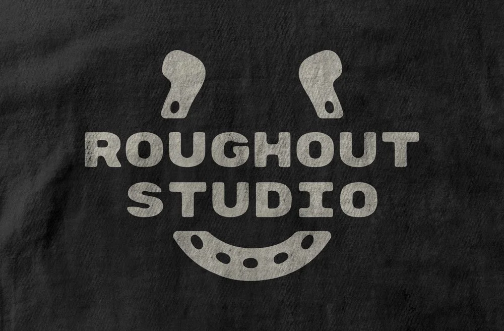 Roughout Studio, Black fabric with a logo for Roughout Studio, featuring two shoe insoles at the top, a smiley face in the middle, and a shoe heel at the bottom.