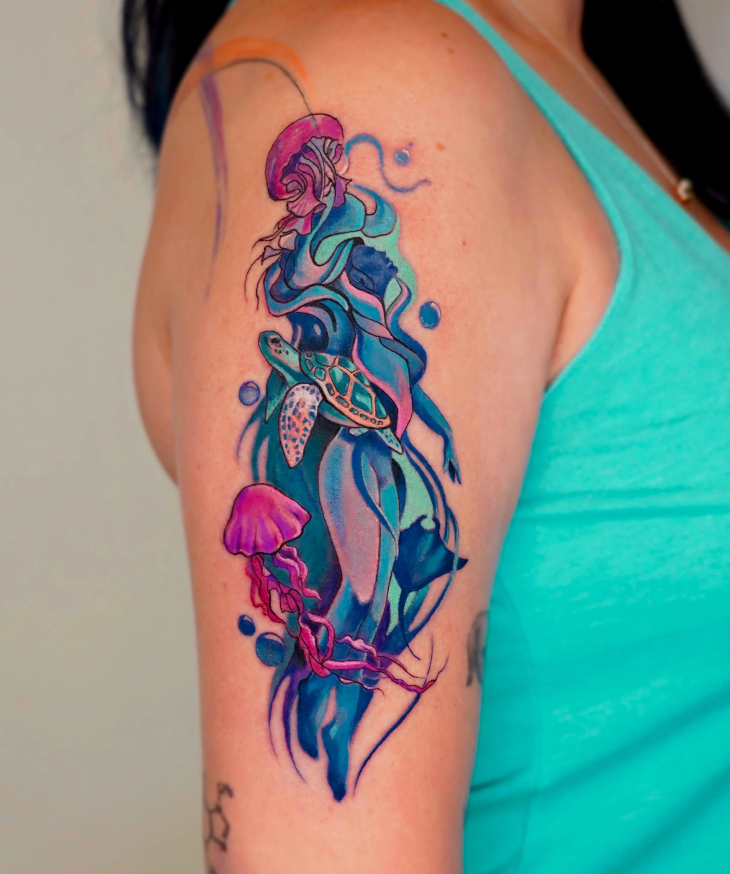 Colorful tattoo of a mermaid with flowing hair, surrounded by jellyfish, a turtle, and bubbles, on person's shoulder.