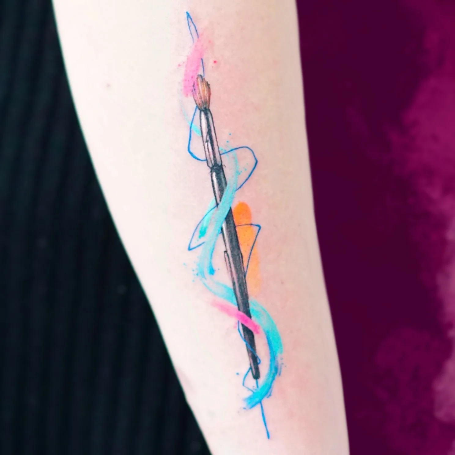 Colorful tattoo of a needle with swirling blue, pink, and orange ink on person's arm.