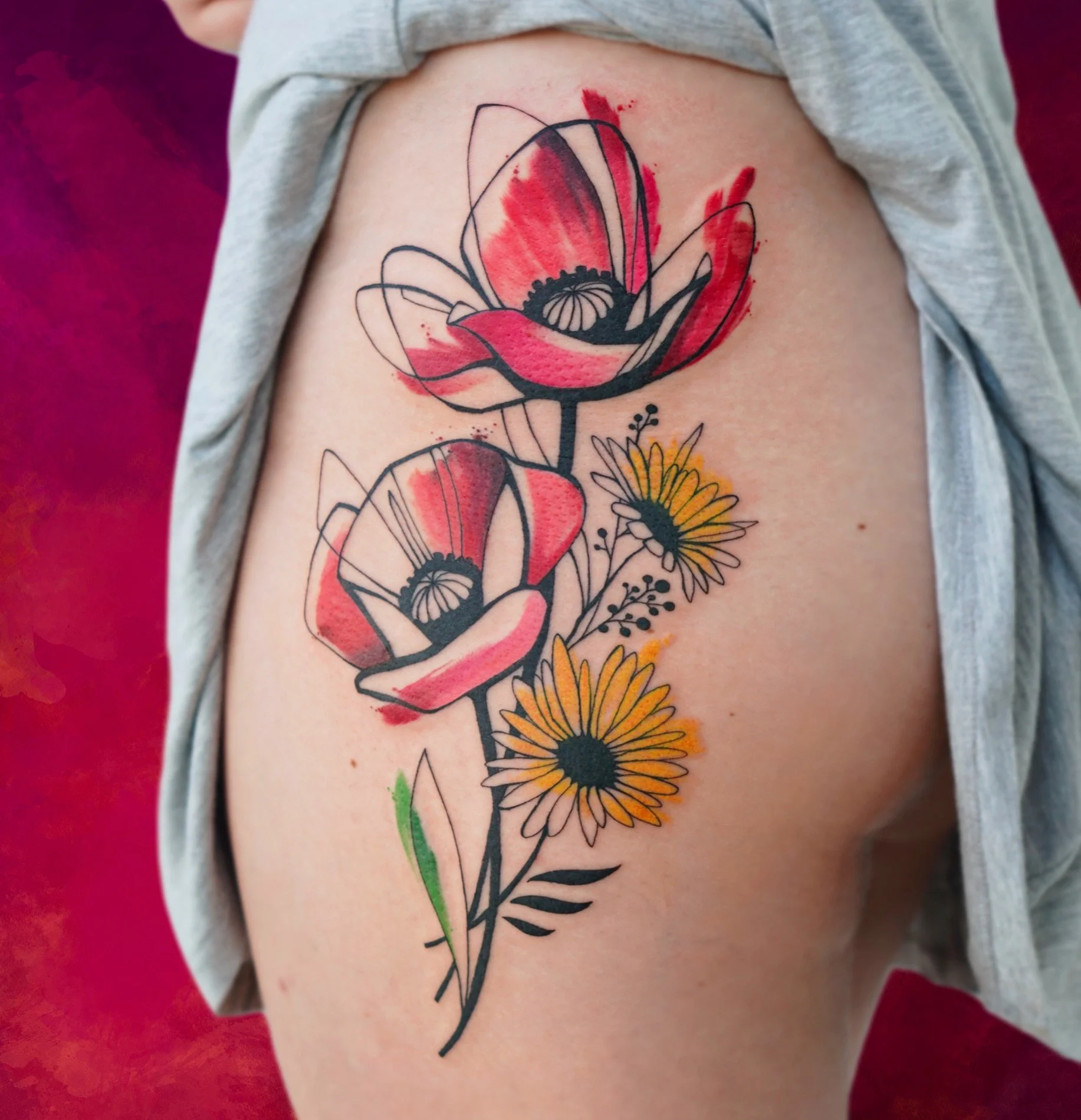 Colorful tattoo of red and black poppy flowers with yellow daisies on a person's upper arm.