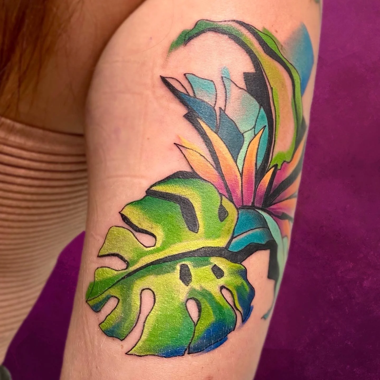 Colorful butterfly tattoo featuring green, yellow, orange, pink, blue, and purple shades on person's arm.