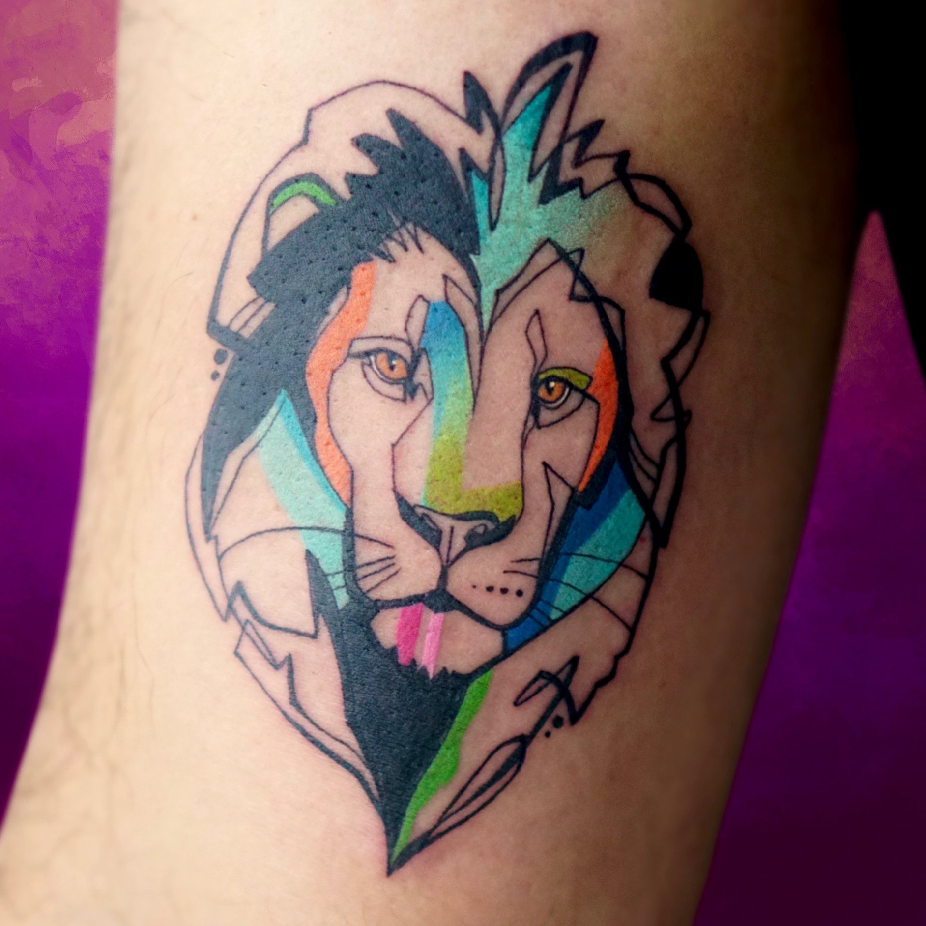 A colorful tattoo of a lion's face with artistic, abstract shading and details on a person's arm.