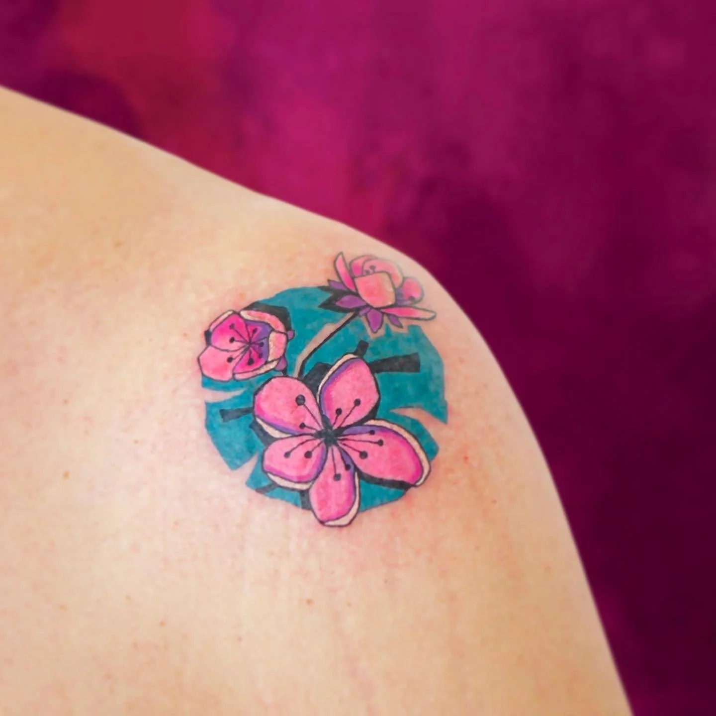 Tattoo of pink flowers and a butterfly with blue background on a person's shoulder.