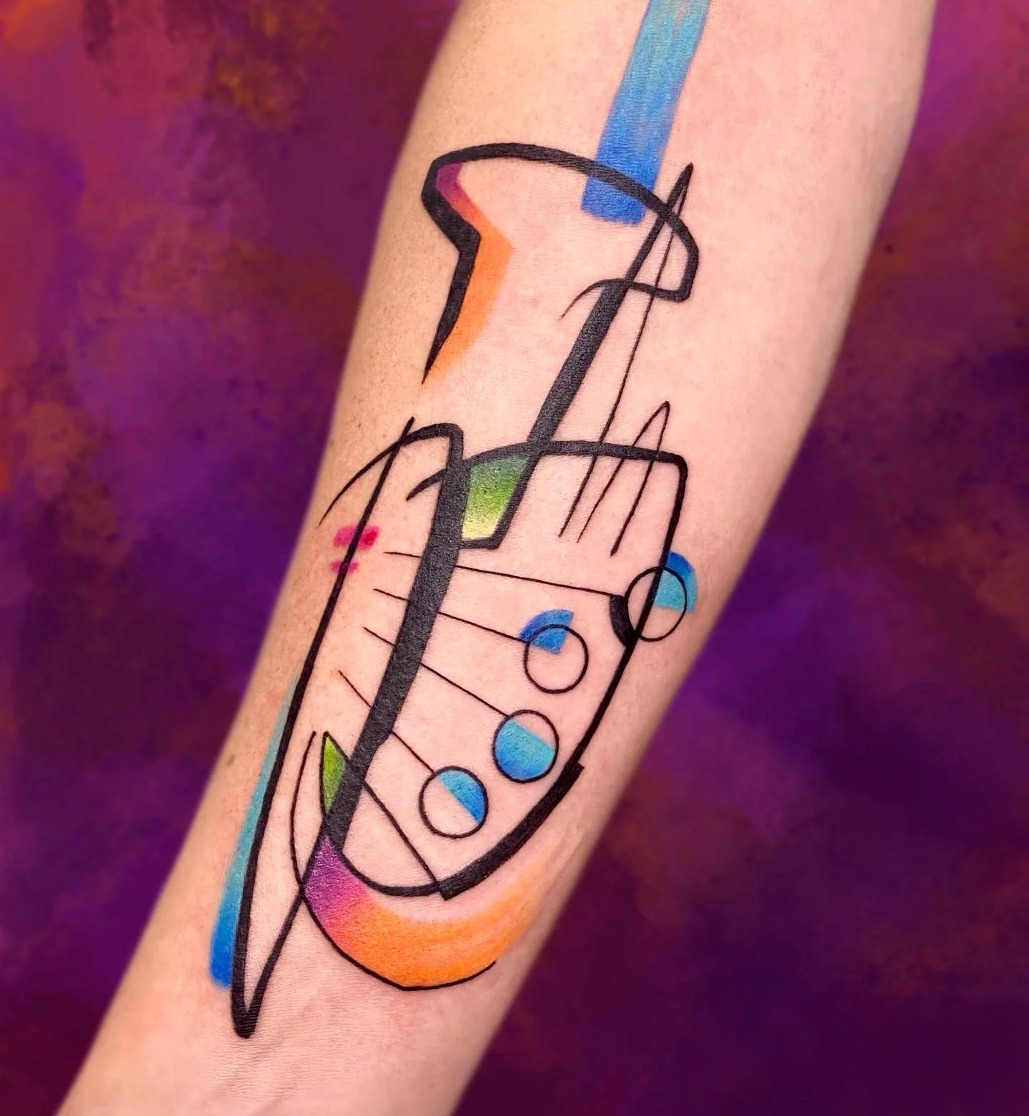 Abstract tattoo design of a syringe with colorful geometric shapes and lines, including shades of orange, blue, green, and pink, on the skin.