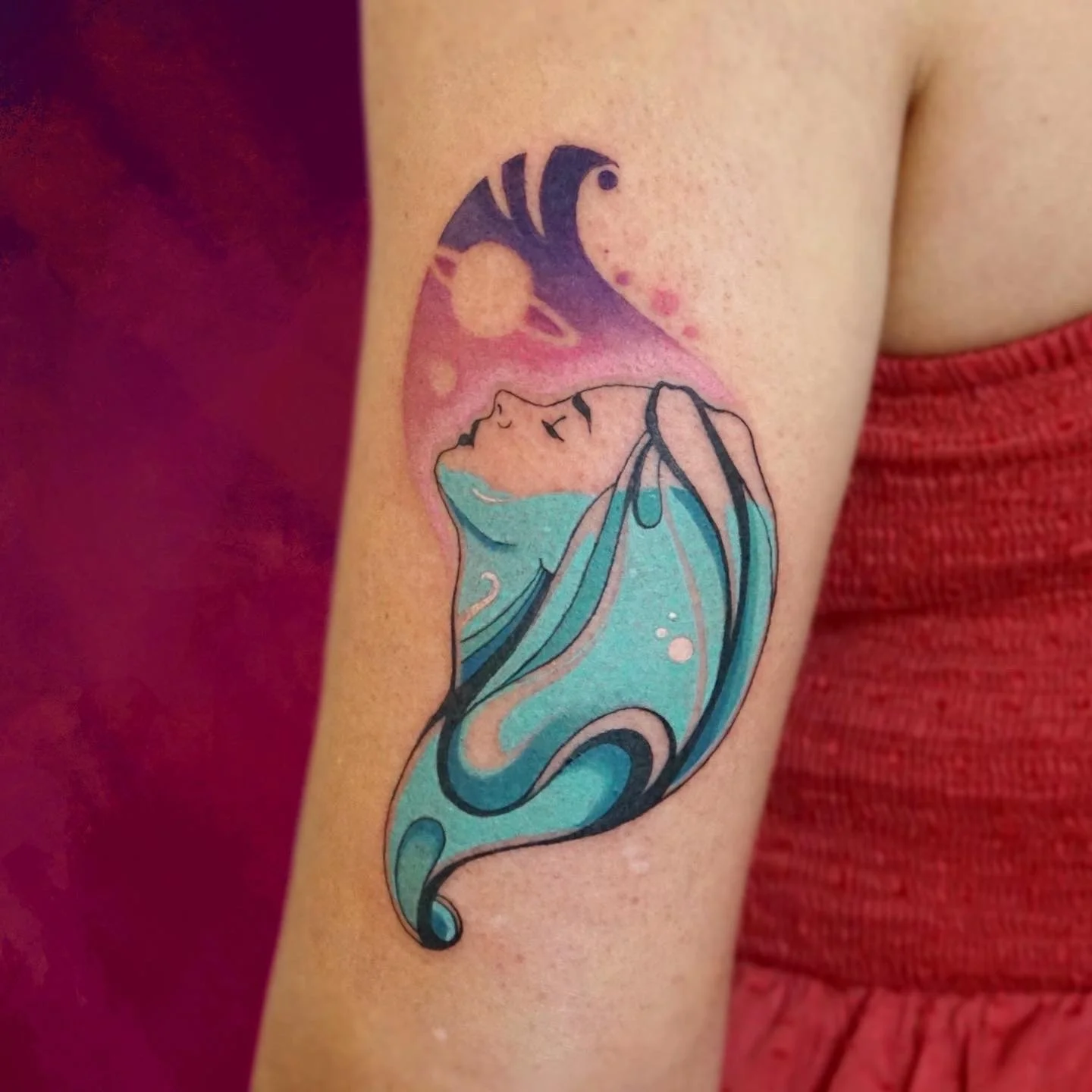 Tattoo of a woman's face with blue hair, surrounded by abstract colored shapes and a black moon on the upper arm.