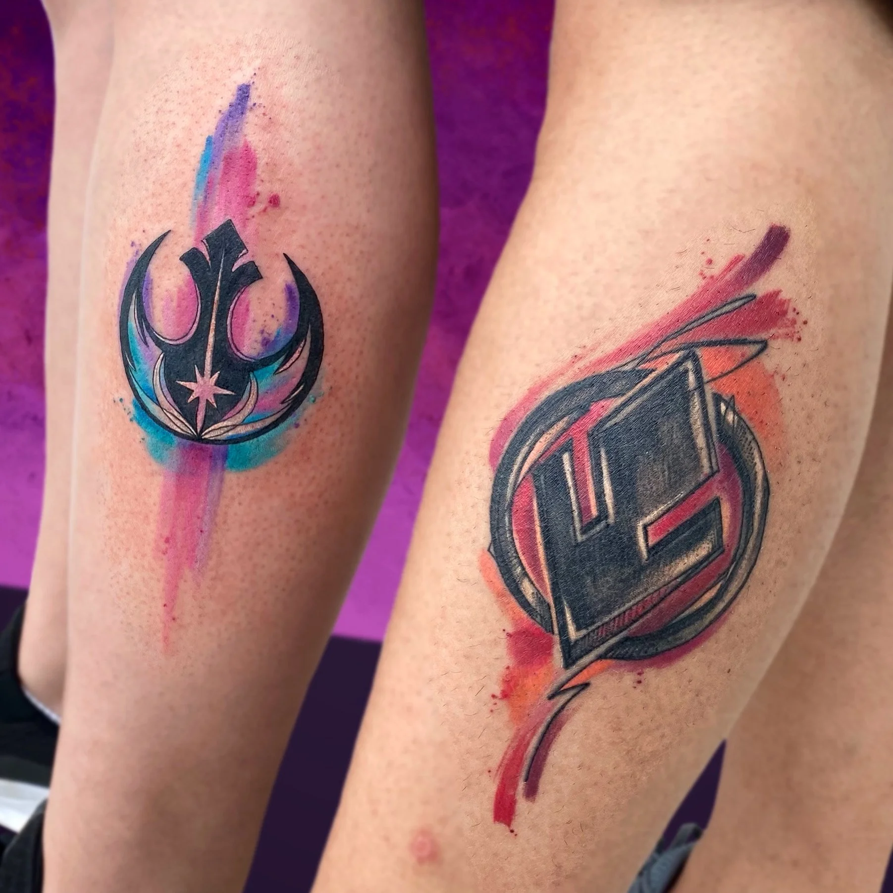 Two upper arms with Freshly done tattoos featuring stylized symbols with watercolor-style background